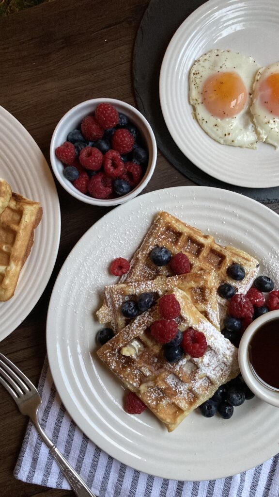 overhead shot of plate full of waffles covered in berries and eggs on the side sunny side up
