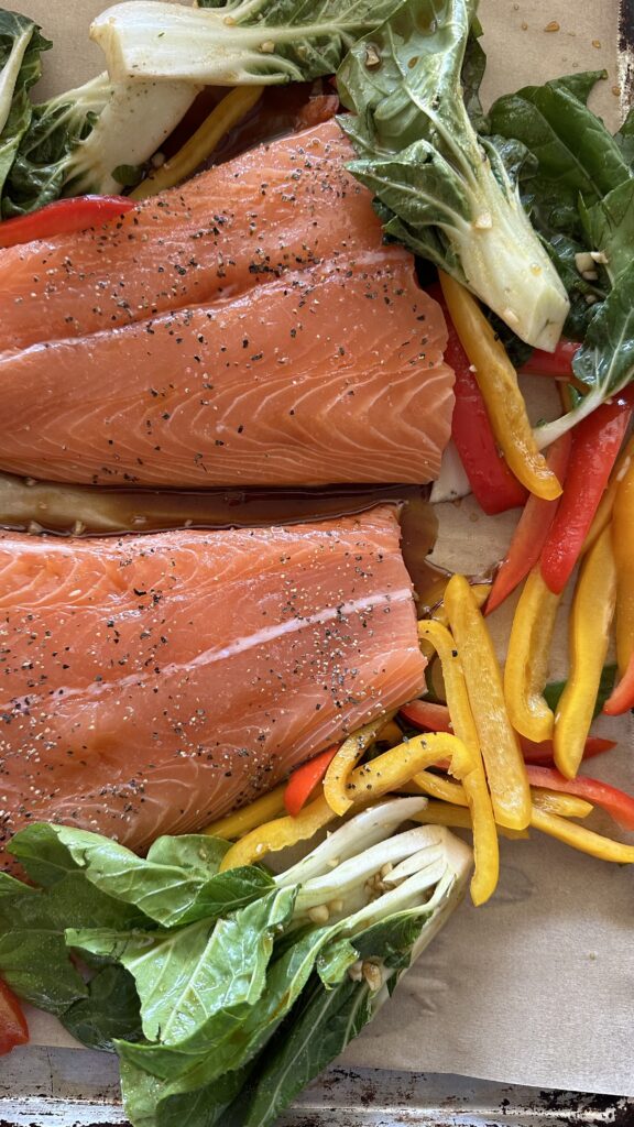 close up photos of fillet of salmon uncooked surrounded by vegetables on a sheet pan