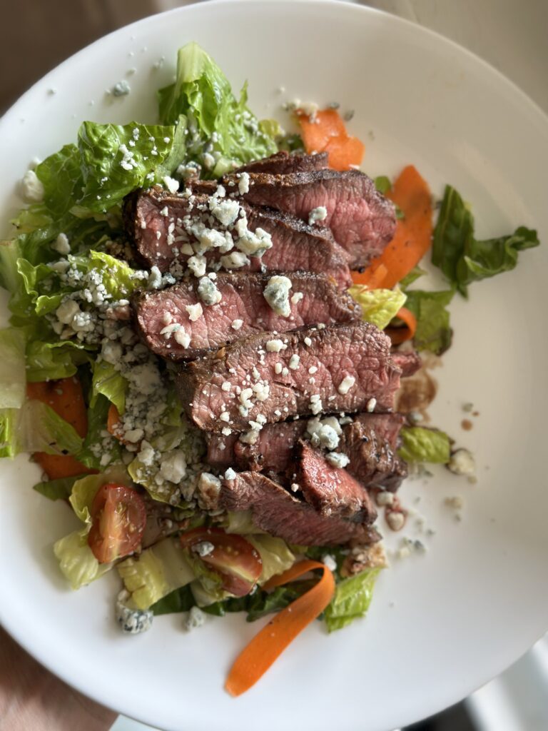 plate with a salad on it topped with steak cuts and crumbly blue cheese