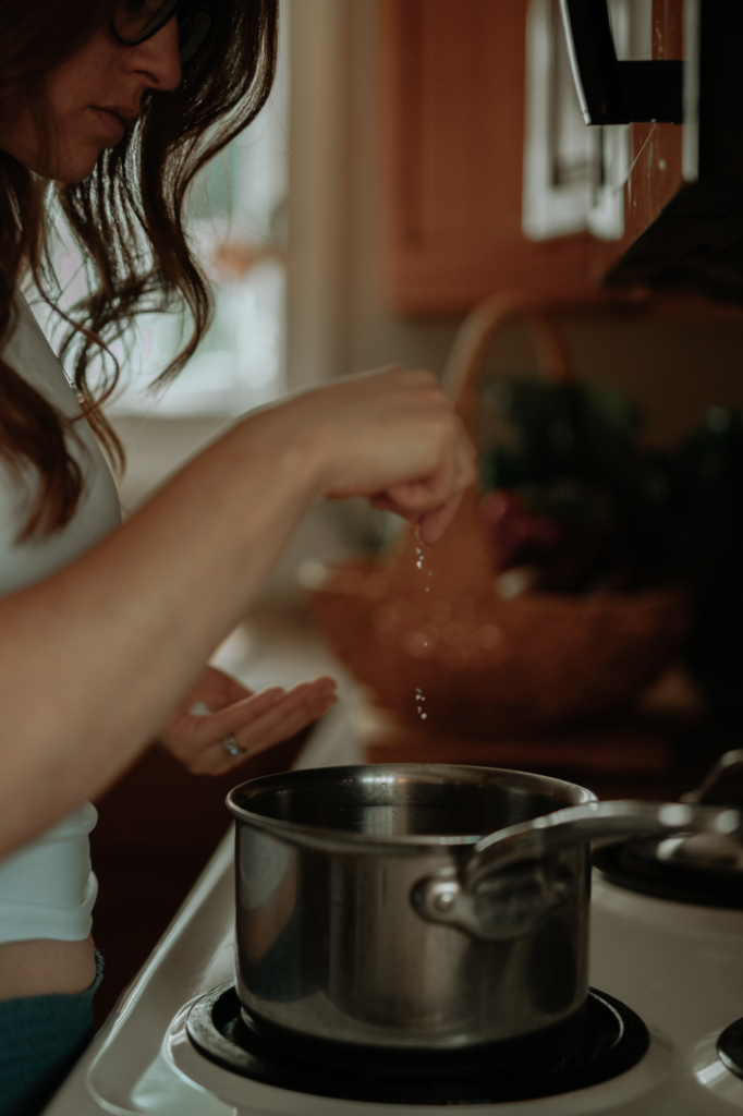 close up shot of woman over stove putting a pinch of salt into a pot