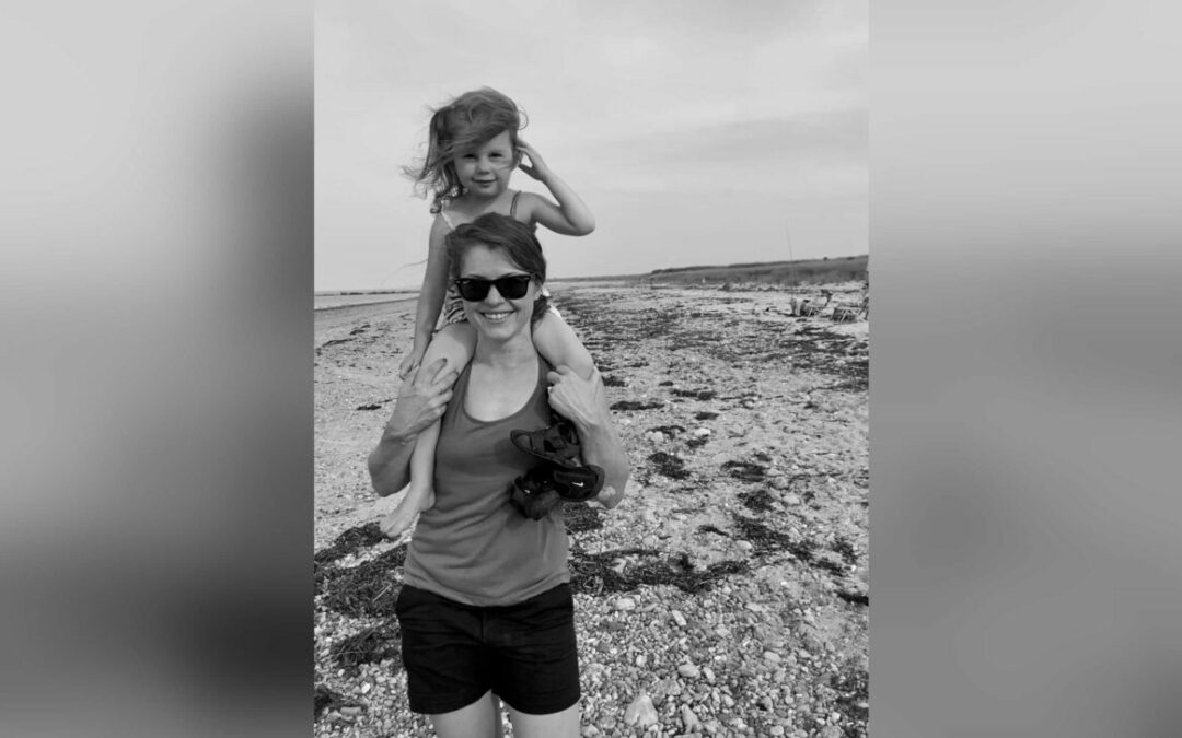 Black and white photo of mother with girl on her shoulders at the beach