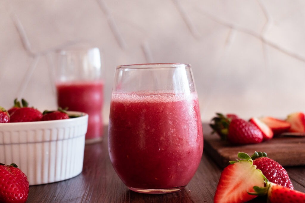 Blended red drink surrounded by strawberries with a second drink in the background