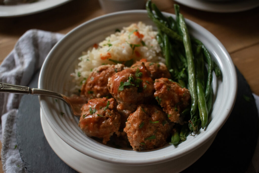 close up show of a bowl full of meatballs, rice and roasted green beans 