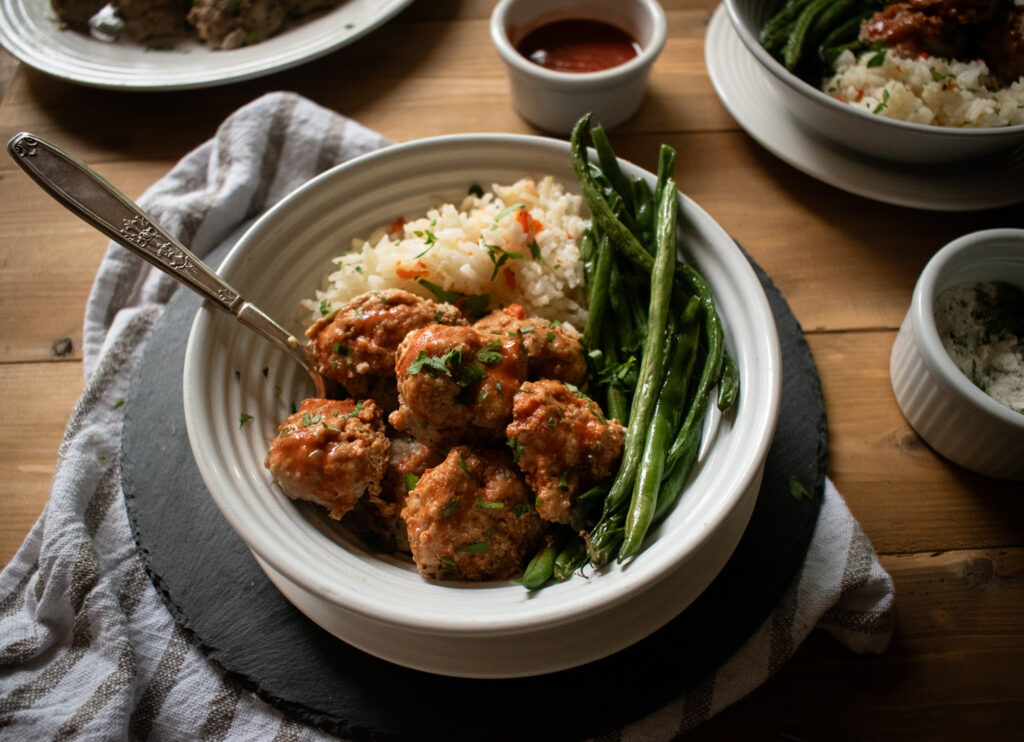 table with Bol of meatballs, rice and green beans with a fork in it