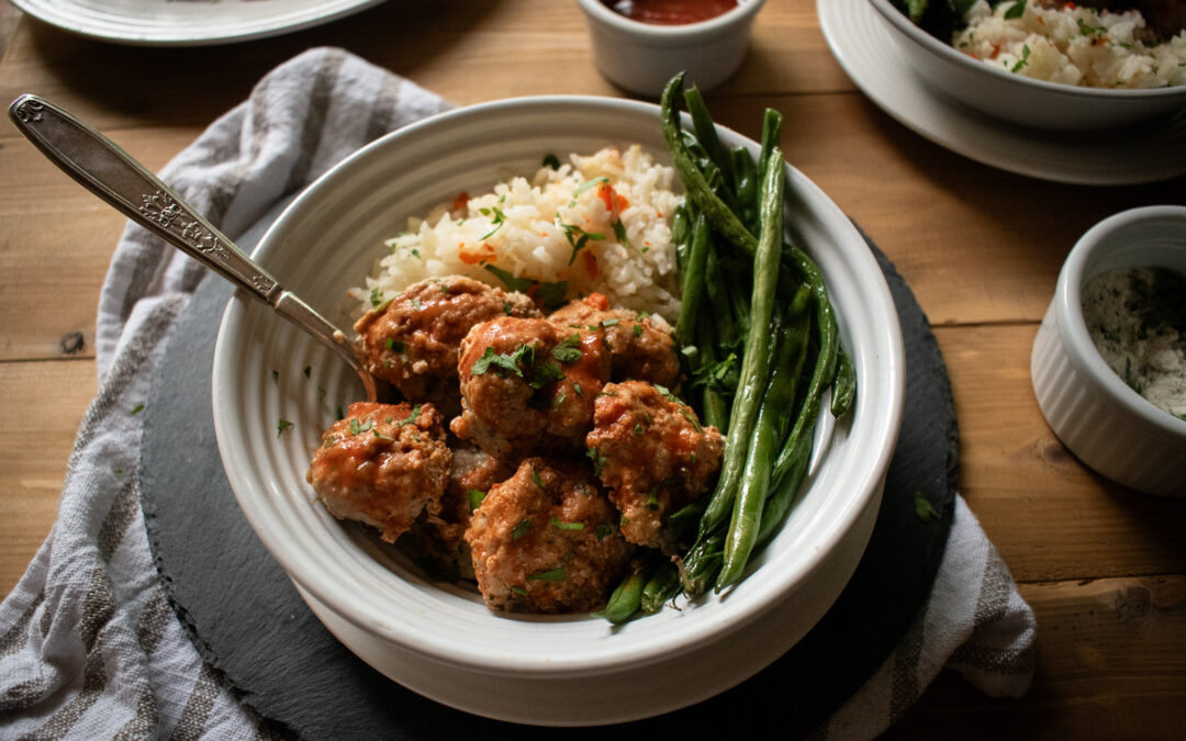 shot of meatballs in a bowl with rice and green beans on a table