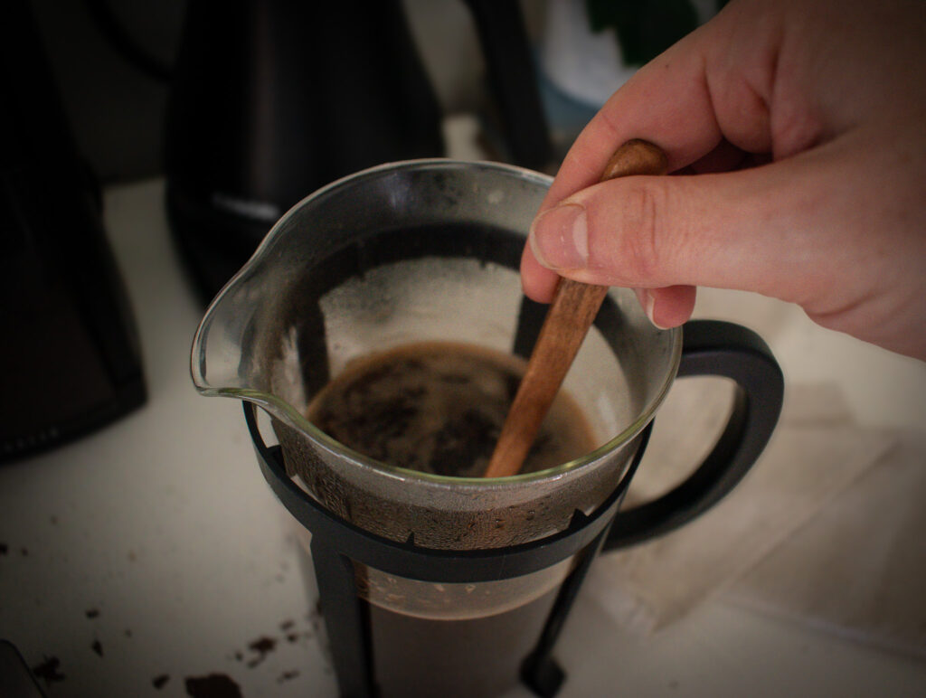 staring a glass French press full of decaf coffee with a wooden spoon