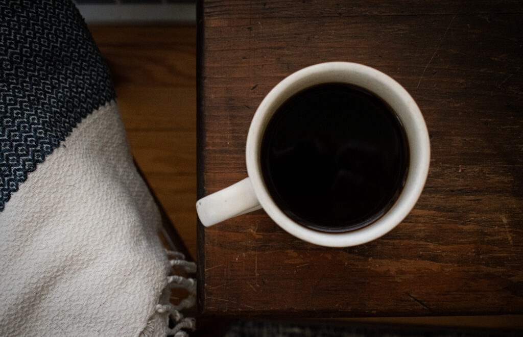 overhead shot of cup of decaf coffee on and end table next to a blue throw blanket 