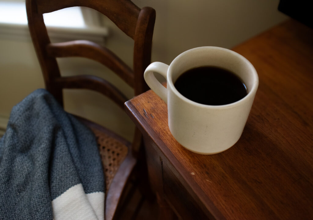 a cup of coffee on end table next to a blanket covered chair