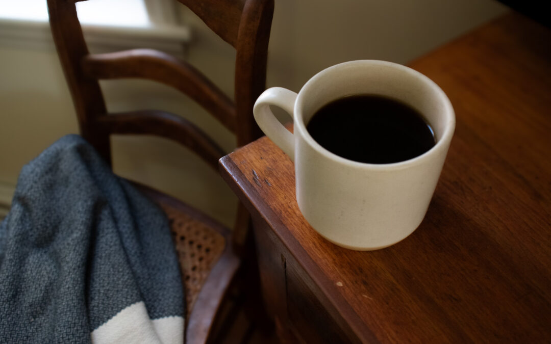 a cup of coffee on end table next to a blanket covered chair