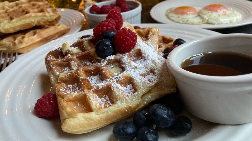 plate of sourdough discard waffles shot from the side with berries and powdered sugar on with a side of maple syrup