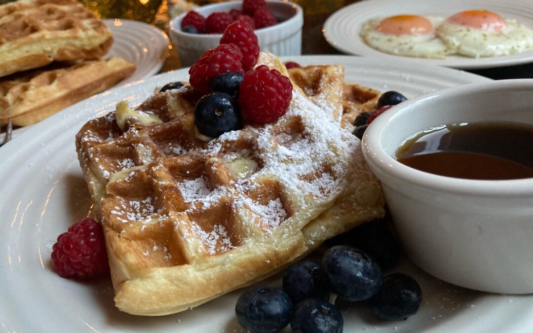 plate of waffles shot from the side with berries and powdered sugar on with a side of maple syrup