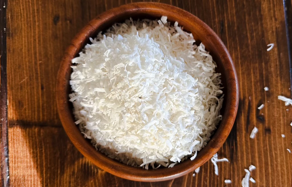 overhead shot of a bowl of coconut flakes on a wooden table 