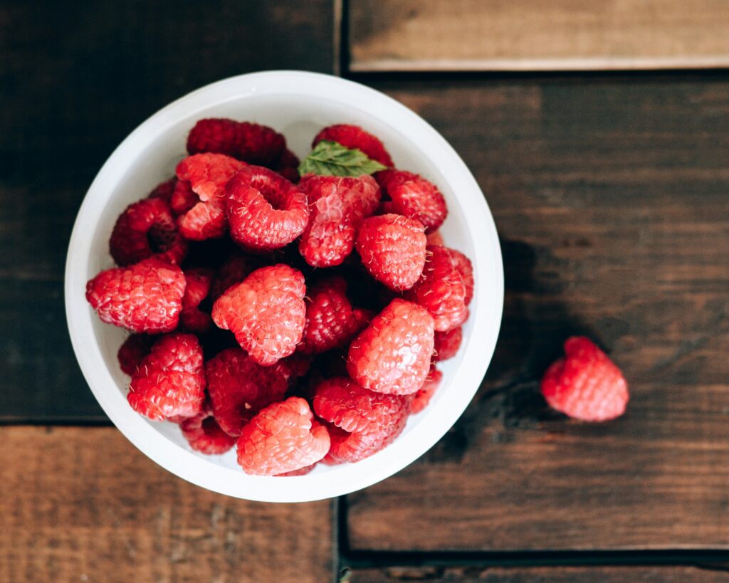 overhead shot of a bowl of raspberries on a wooden table