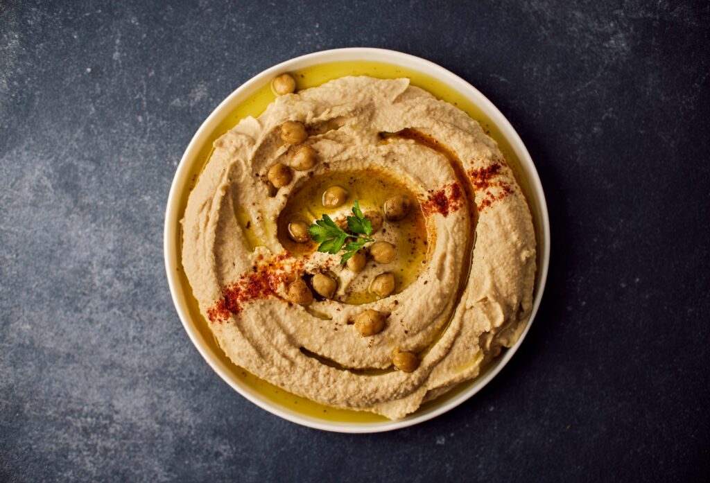 overhead shot of a bowl of hummus sprinkled with pint nuts and olive oil