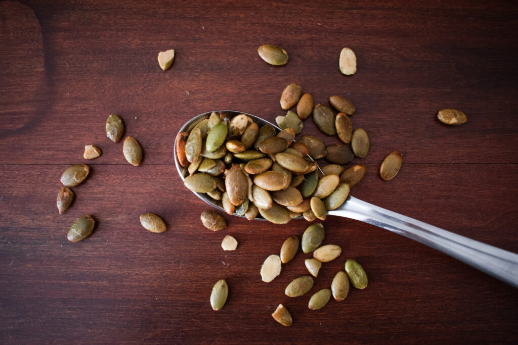 A spoon on a wooden table holding pumpkin seeds