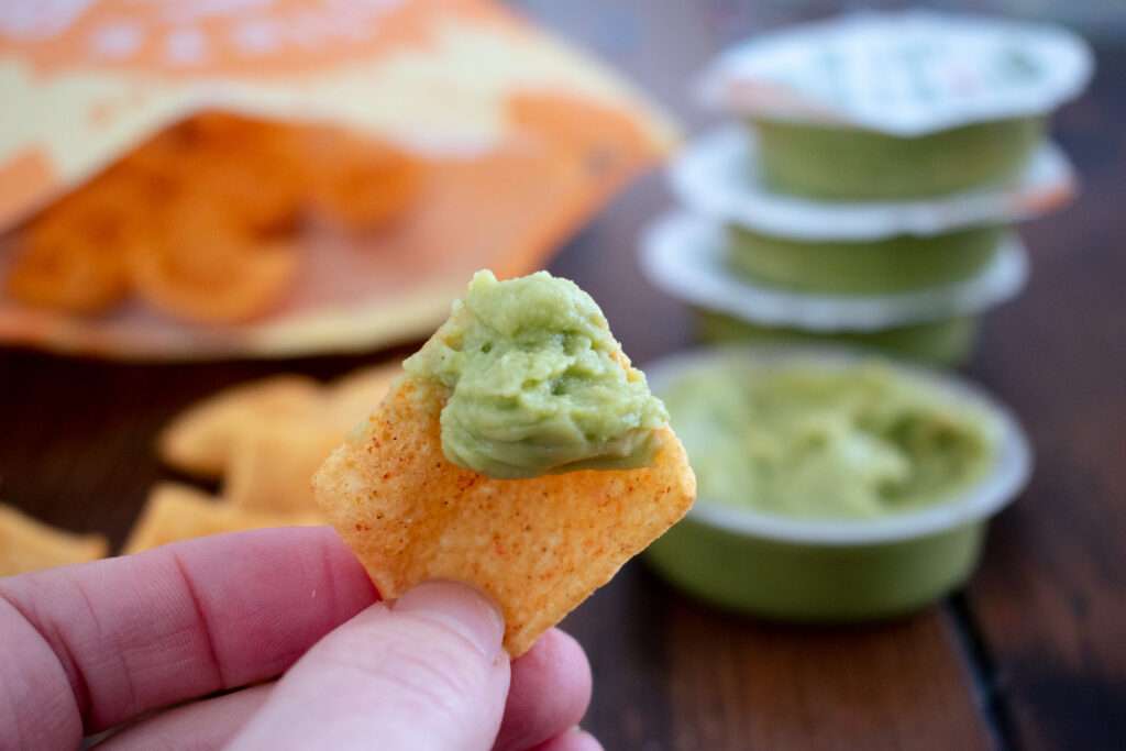 a hand holding a chip cover in guacamole with guacamole in the background