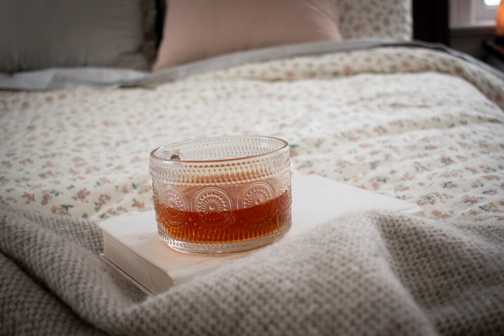 cup of tea setting on a book on top of a flowered bed spread 