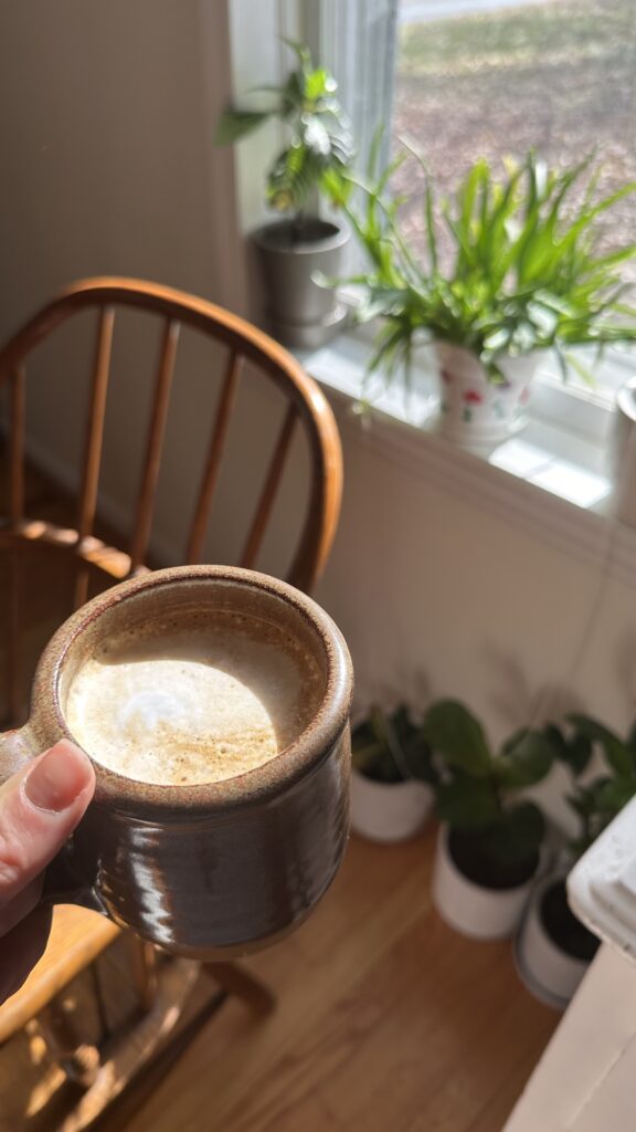 hand holding a cup of mushroom coffee over some house plants