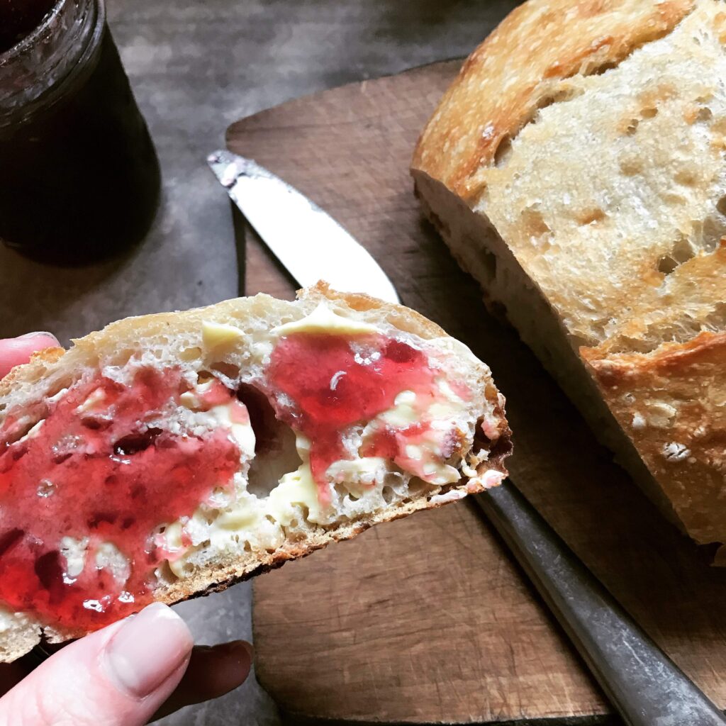 hand holding a piece of crusty bread with butter on it