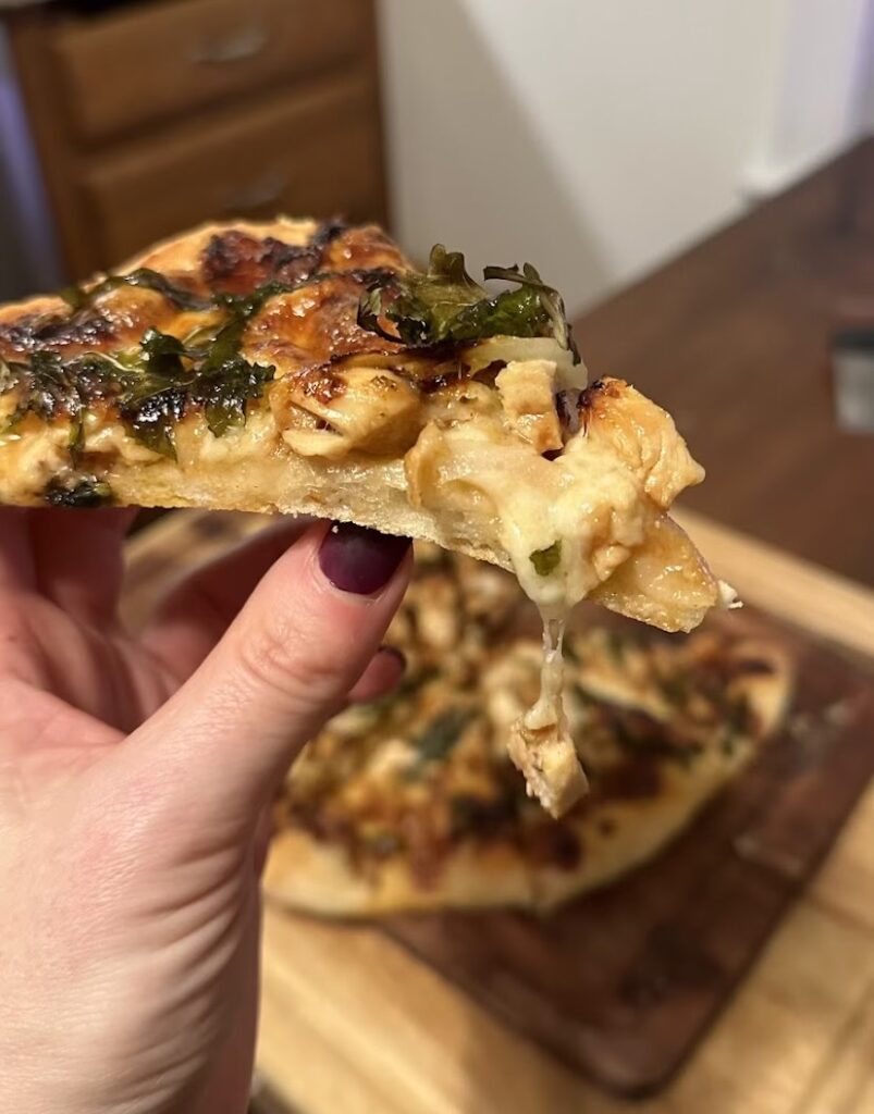 hand holding a piece of bbq chicken pizza on sourdough crust