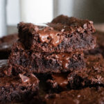 stack of chocolate brownies with melted chocolate and a glass of milk in background