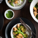 overhead shot of a few plates of sesame chicken with chopsticks and green onions