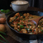 Thai chicken curry in a skillet surrounded by produce