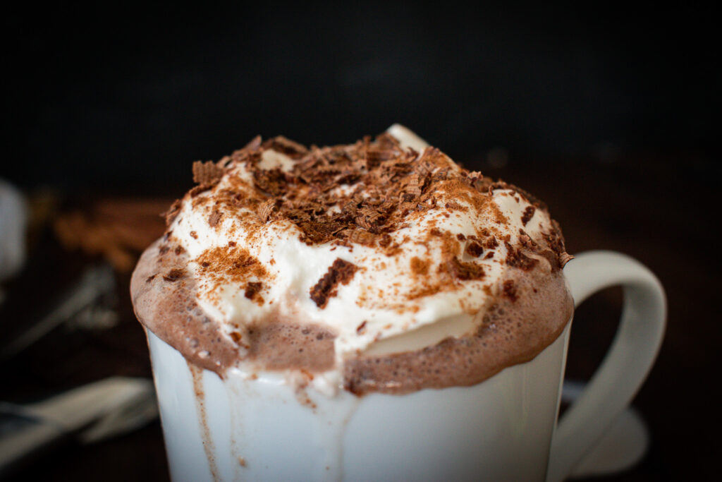 close up of hot cocoa with whipped cream and chocolate shavings with a sip taken out of it 