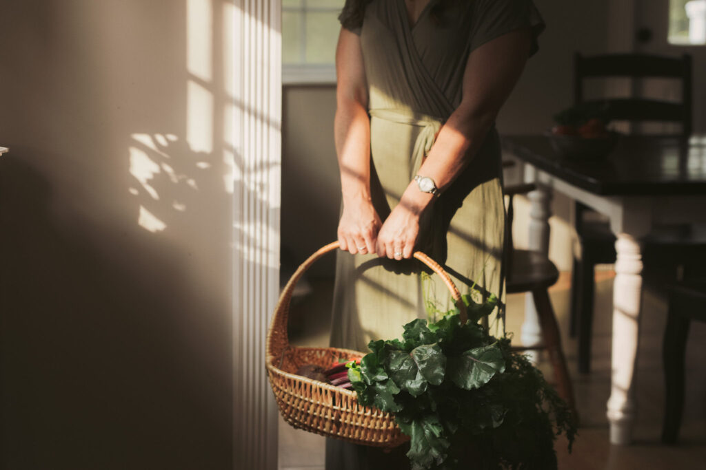 woman in green dress standing in sunlight holing basket full of leafy greens